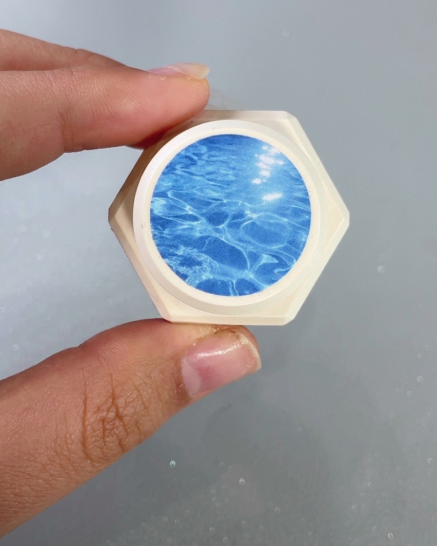 A close-up of a nail brush applying a clear blue glass gel onto the tip of the nail.