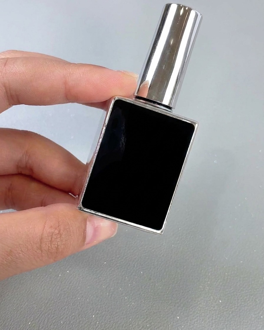 A square black and silver bottle of nail top coat being held by hand against a neutral background.