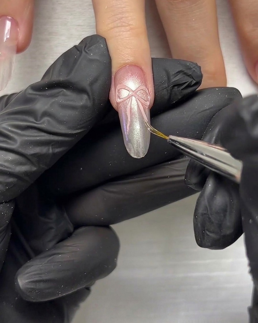 A close-up of a detailing tool being used to press and shape 3D ribbon elements on a nail.