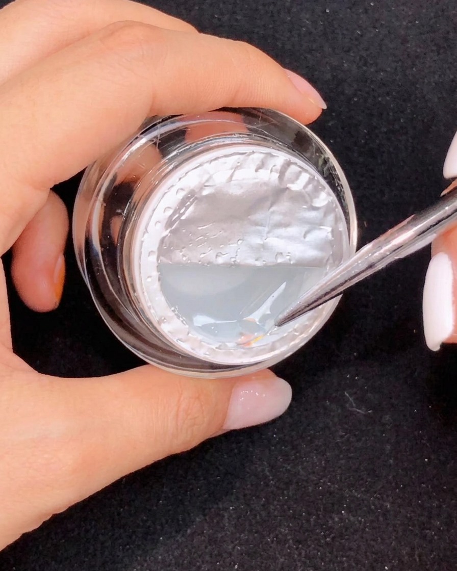 A fine brush pulling a long teardrop shape of clear gel on an ombre pink nail.