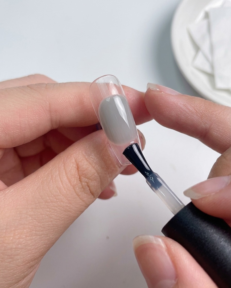 A brush applying a layer of top coat over a colored nail.