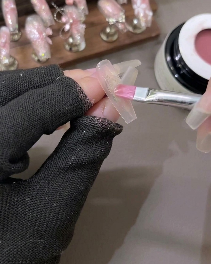 A brush softly blending a sheer red gel color onto the center of the nail to create a gradient effect.