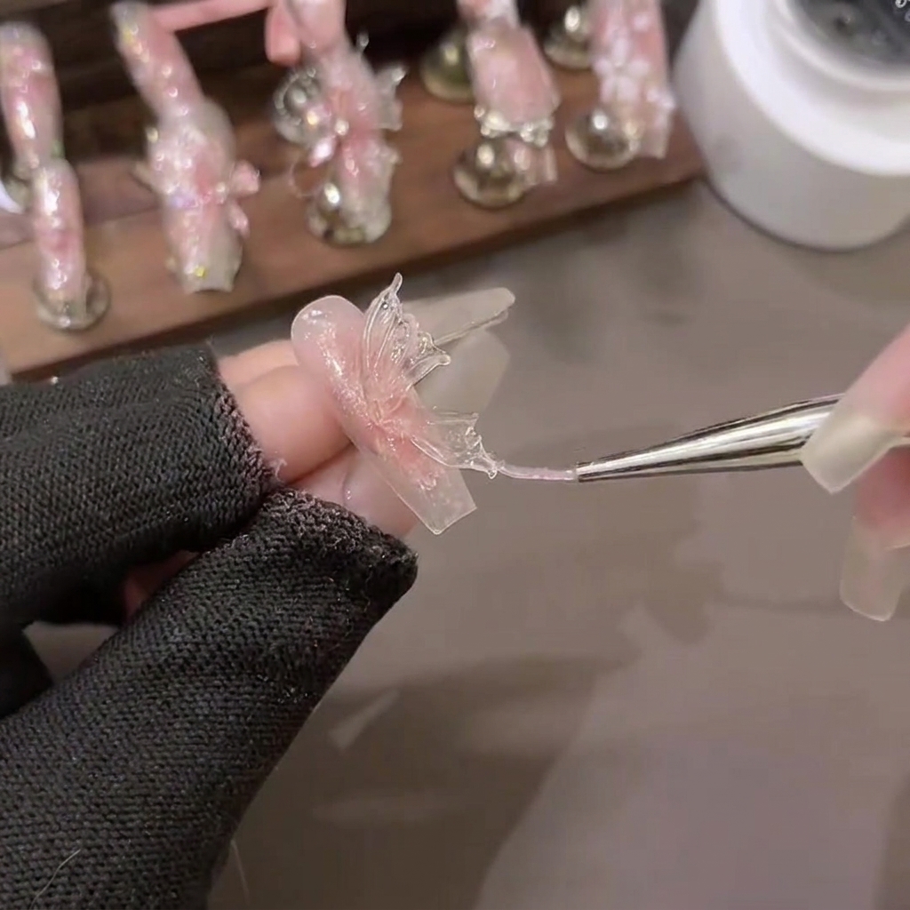 A carving brush shaping a triangle of PVC soft extension gel into detailed butterfly wings on backing paper.