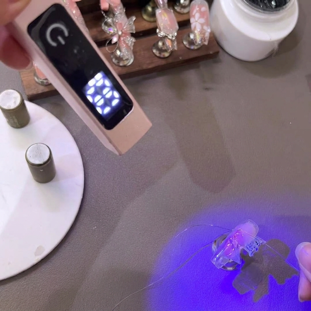 Tweezers pulling and shaping the delicate tips of a PVC gel butterfly wing under a mini UV lamp.
