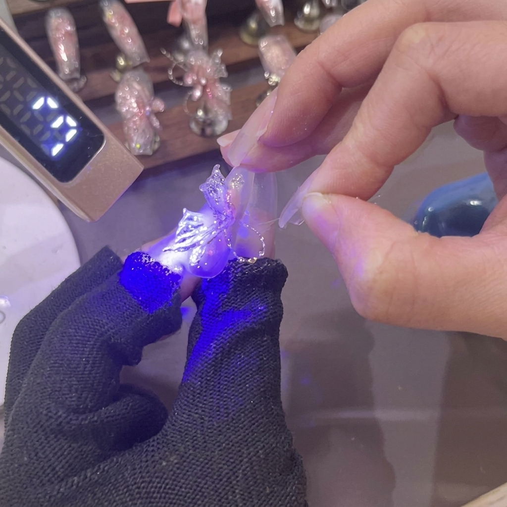 A mini UV lamp shining purple light over a newly shaped 3D pink gel butterfly wing on a fingernail.