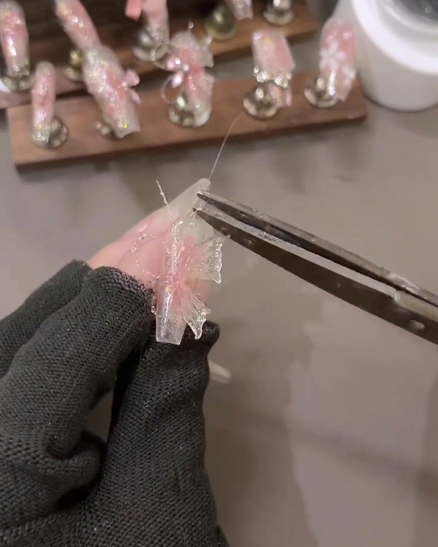 A close-up of a hand applying shattered diamond glitter gel details onto a 3D nail art design with tools nearby.