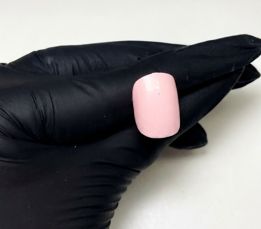 A close-up of a prepped pink nail with a single small dot of pink builder gel placed in the upper center.