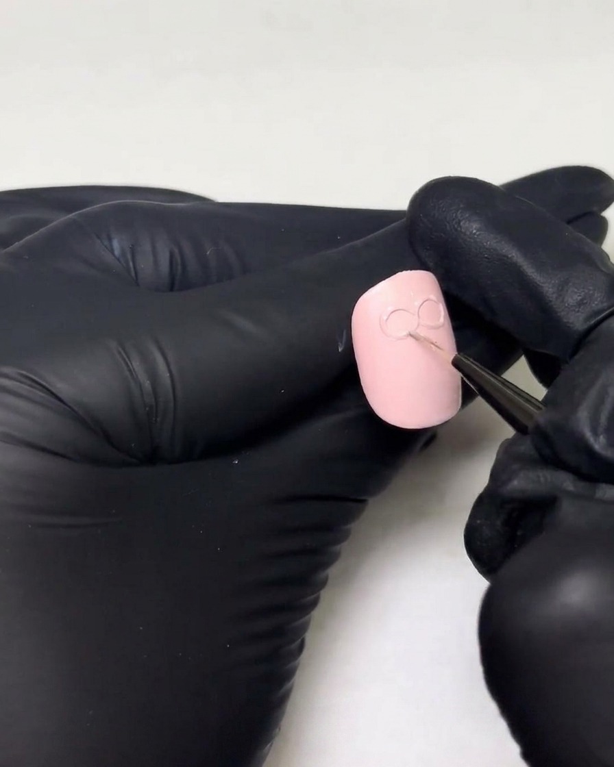 Gloved hands adding a thicker layer of builder gel over the existing loops of a 3D bow design on a nail.