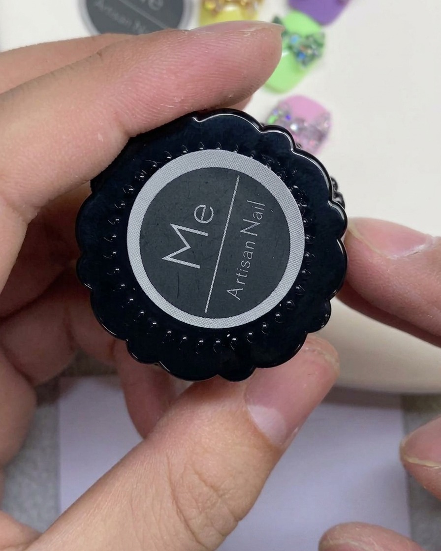 A hand holding a black jar labeled Artisan Nail with a white circular logo.