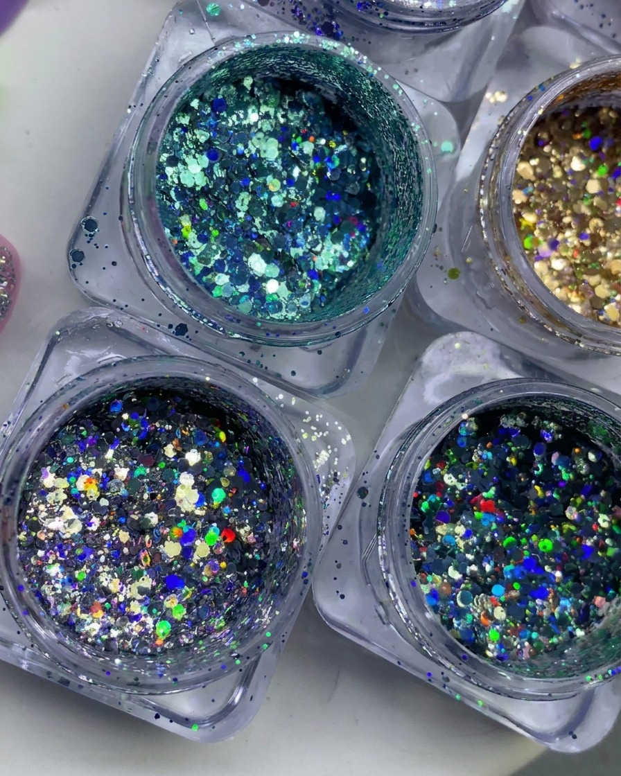 An overhead view of multiple small jars filled with colorful, holographic, and metallic glitter flakes.