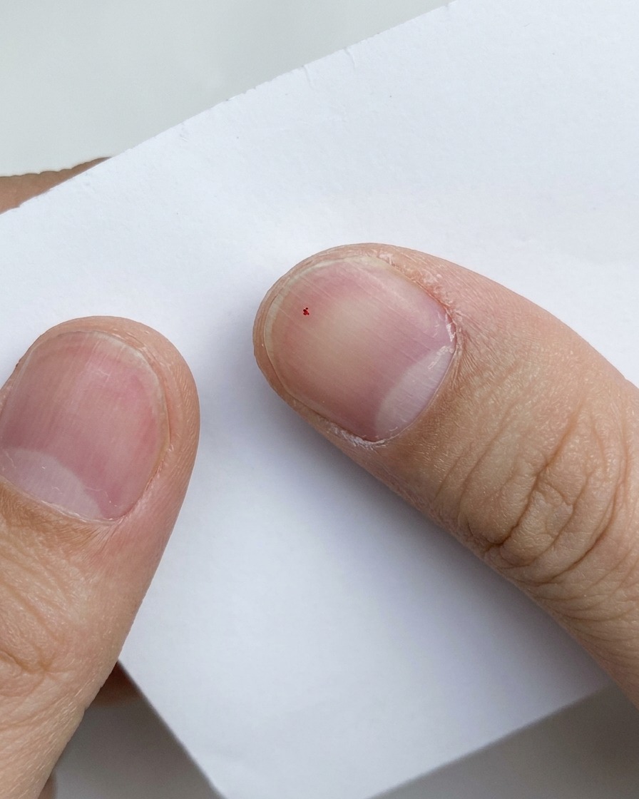 A close-up view of a tiny speck of purple glitter mixed onto a white paper background.