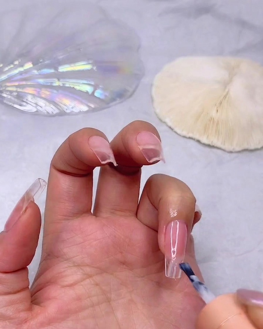 A brush applying a layer of milky white gel polish to the tip of a pink-toned nail to start an ombre effect.
