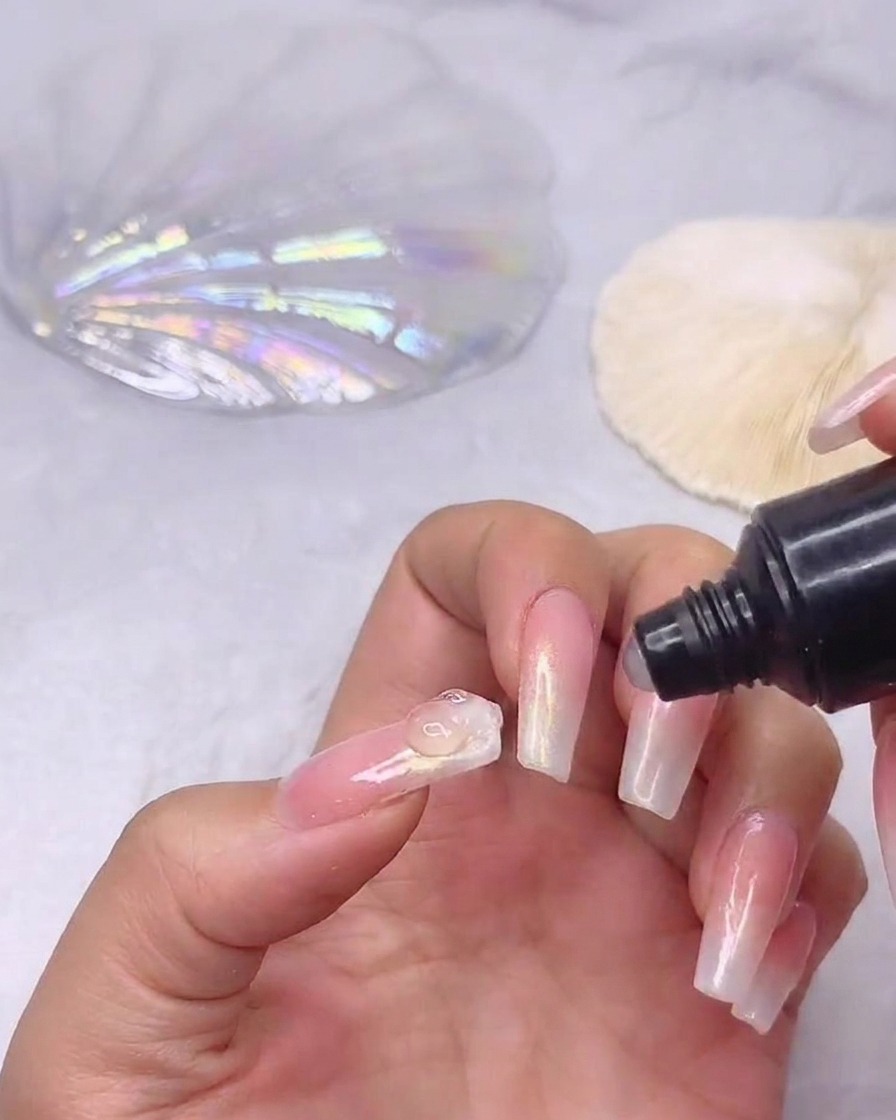 A tube of rhinestone gel adhesive dispensing a small clear bead of glue onto the center of a prepped gradient nail.