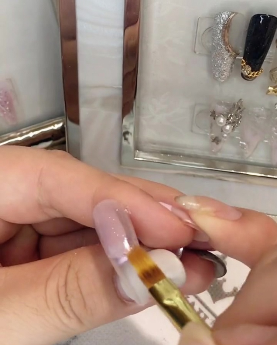 A flat nail brush blending pink gel downwards on the center of the nail plate.