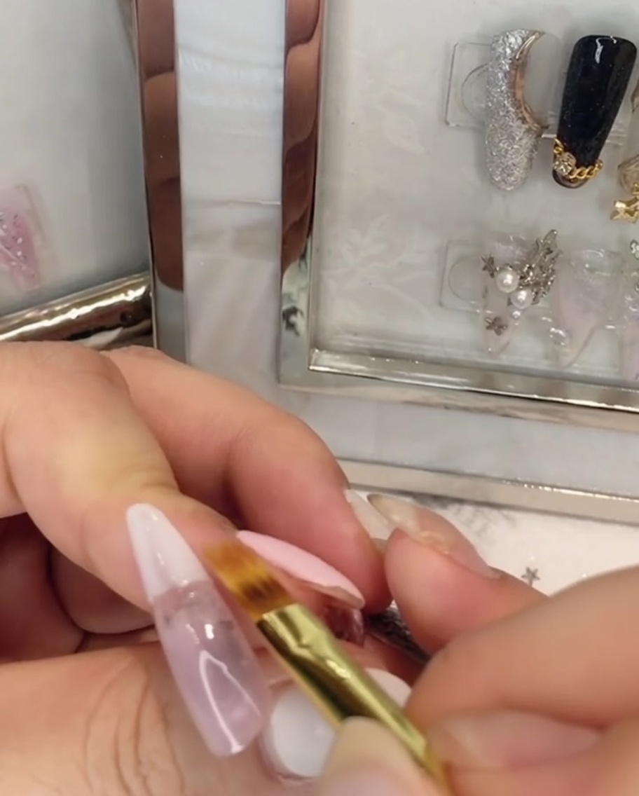 A flat brush blending white gel polish upwards into the pink gel on the nail.