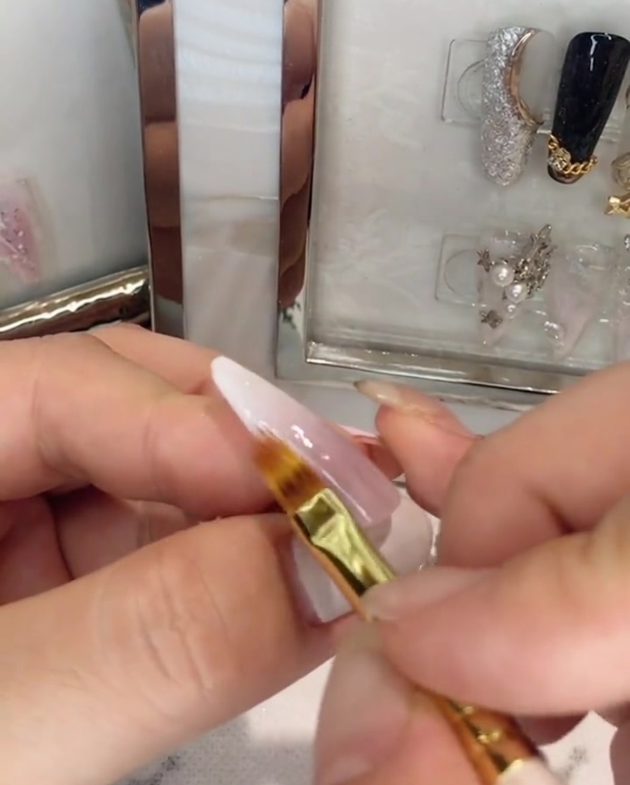 A brush applying clear top coat over a pink and white ombre nail.