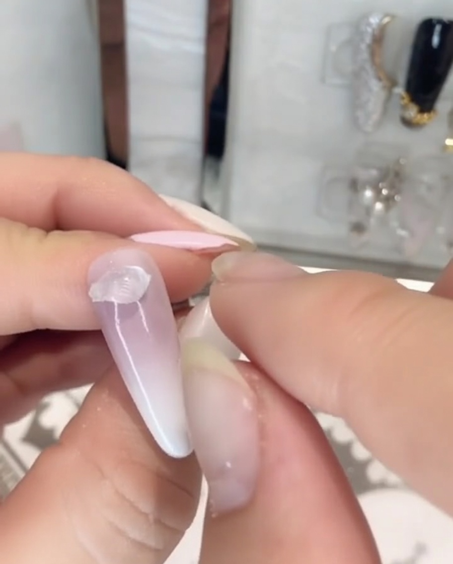 Fingers placing a piece of clear, thick solid rhinestone glue onto the base of a painted nail.