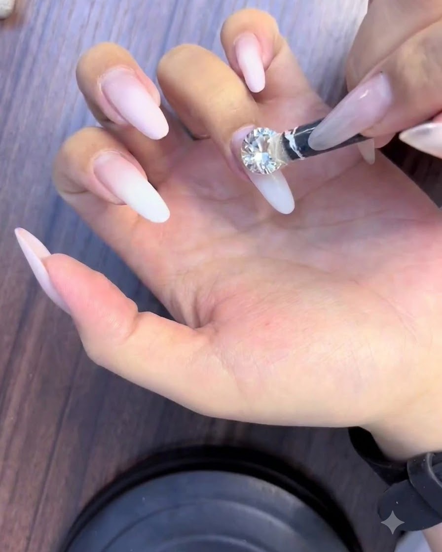 A pickup tool placing a large sparkling diamond rhinestone onto the center of a nail.