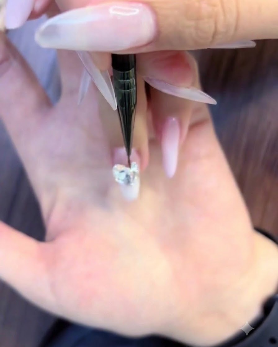 A fine nail art brush placing tiny round rhinestones around the lower edges of a large crystal cluster.