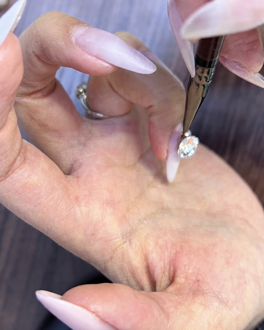 A fine detail tool placing microscopic round rhinestones into the tiny gaps beneath a large nail crystal.