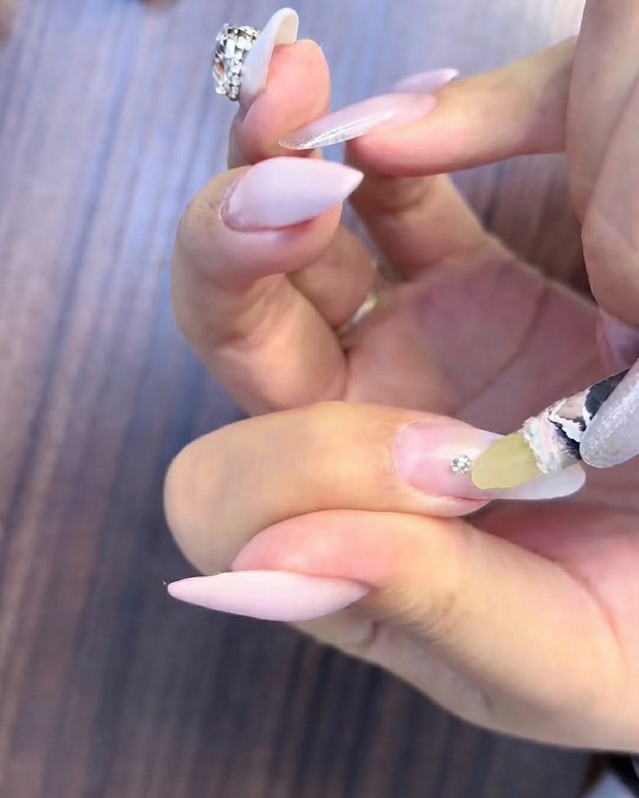A fine brush applying clear filling gel around the base of a small rhinestone cluster on a gradient nail.
