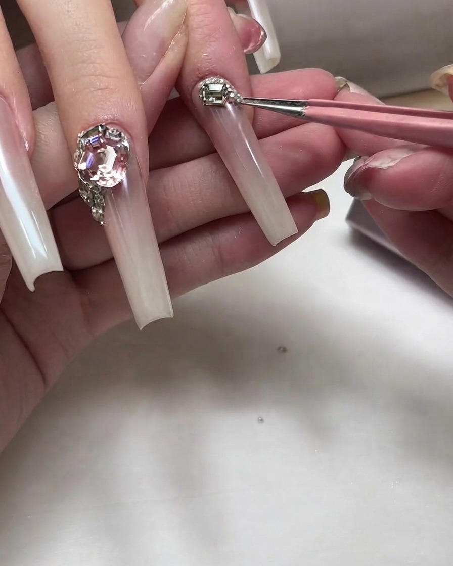Precision tweezers placing small silver metal studs and micro rhinestones near the nail cuticle.