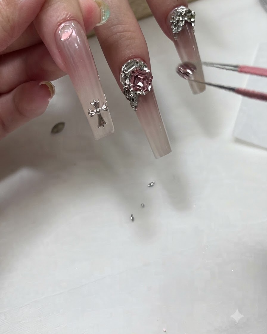 A manicurist using tweezers to place a small crystal charm near the base of a long ombre nail.