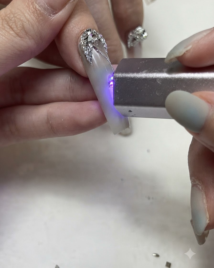 A portable UV/LED flashlight curing fine silver gel lines and rhinestone details on a decorated nail.
