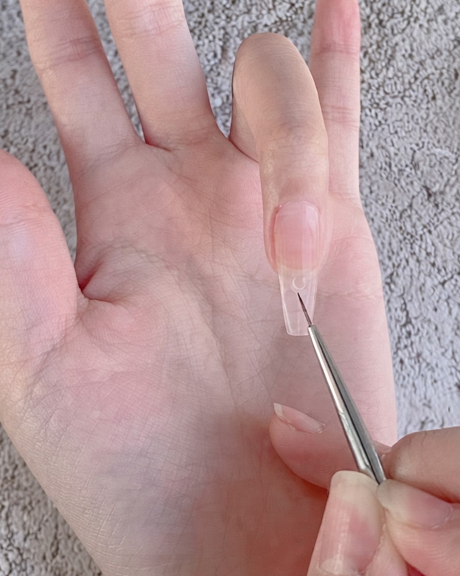A fine nail art liner brush placing a small clear bead of rhinestone gel onto a nude gel-coated nail.