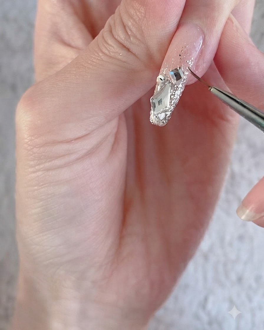 A fine liner brush outlining large sparkling crystal rhinestones and charms on a decorated nail surface.