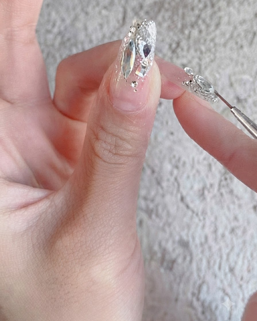 A nail brush applying a glossy reinforcement top coat over a fully finished rhinestone nail design.