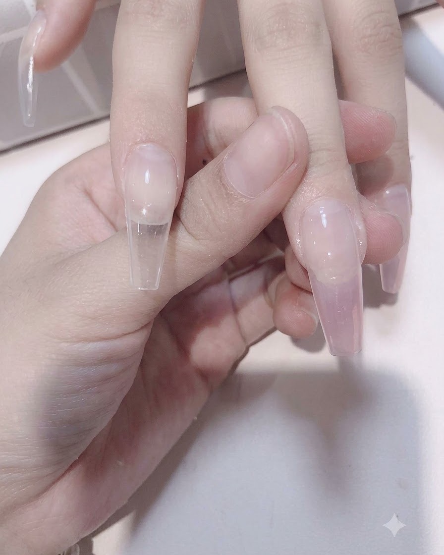 A nail brush blending sheer pink gel downward over a translucent nail extension to form a gradient effect.