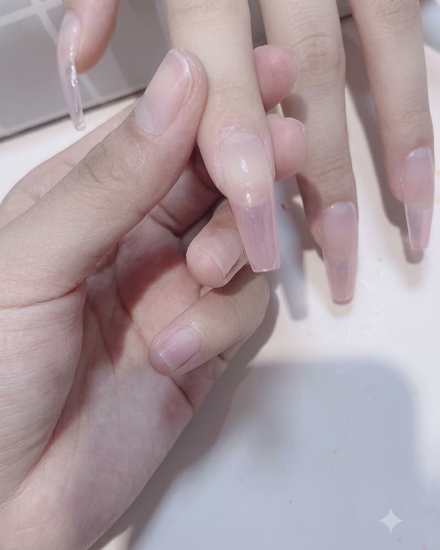 A close-up view of fingers showing the second application of sheer pink gel building the gradient depth.
