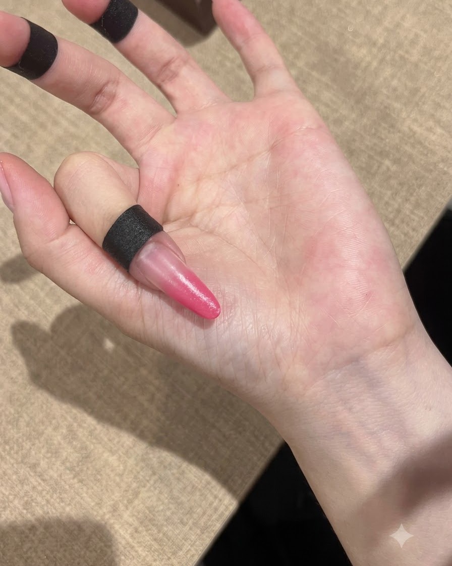 A hand positioned under a compact UV lamp to cure the pink gradient nails.
