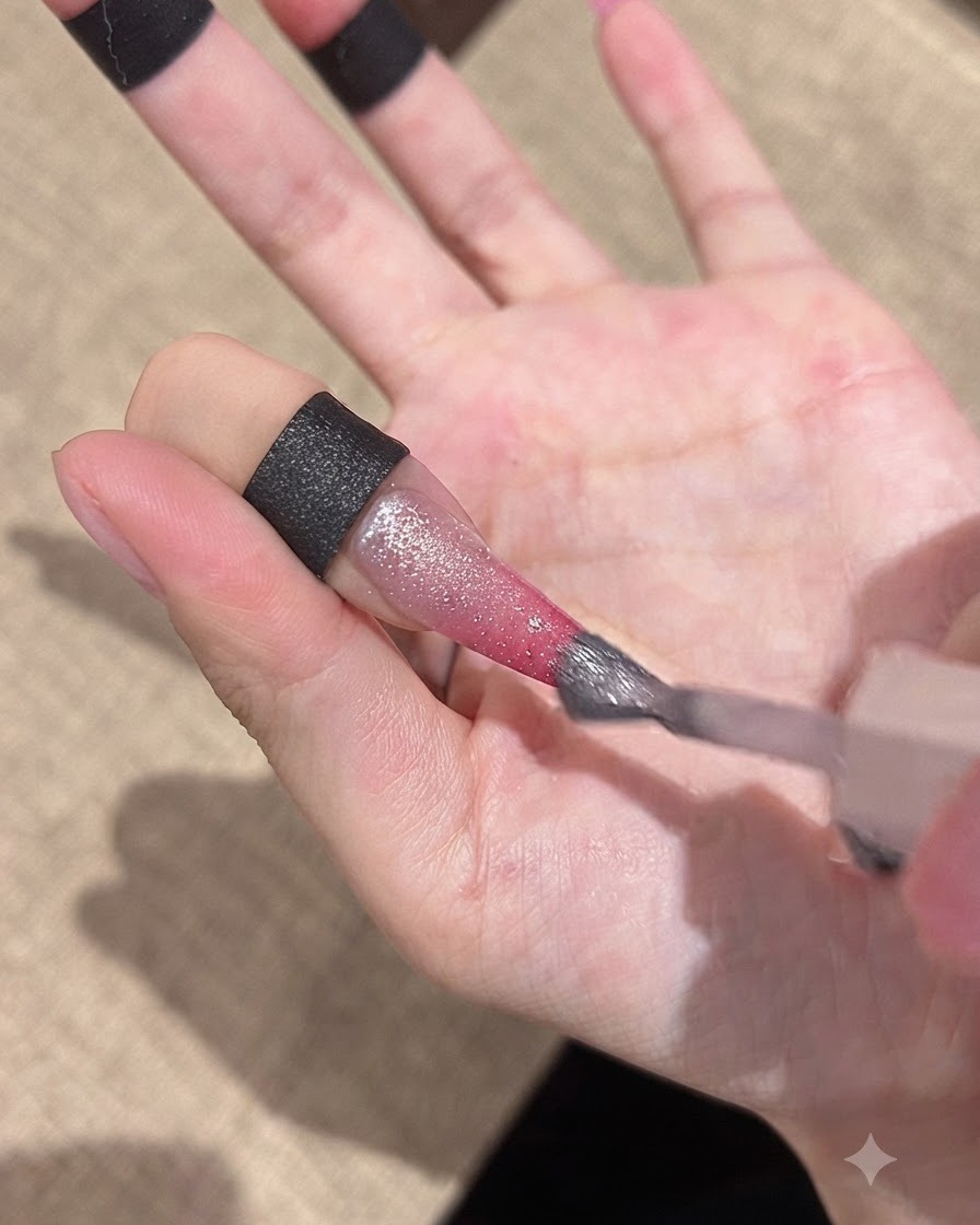 A brush applying a sparkly cat-eye gel over the gradient nail surface.