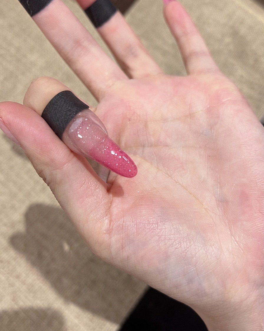 A close-up view of a nail showing fine reflective glitter particles under standard indoor lighting.