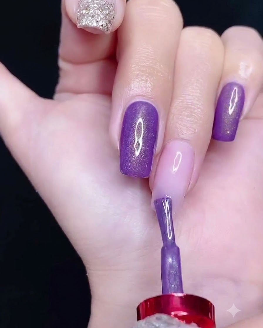 A brush applying purple gel polish to the upper section of a nail.