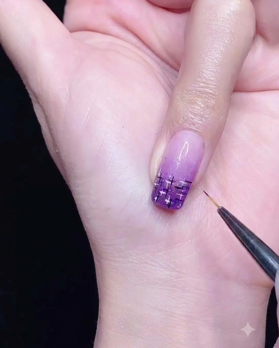 A fine liner brush drawing intersecting black and silver lines on a purple gradient nail.