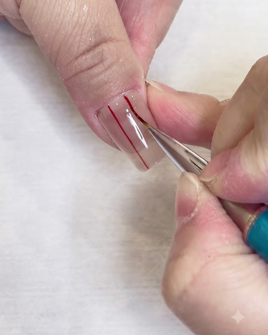 A fine liner brush drawing a second parallel red vertical line on a clear nail.