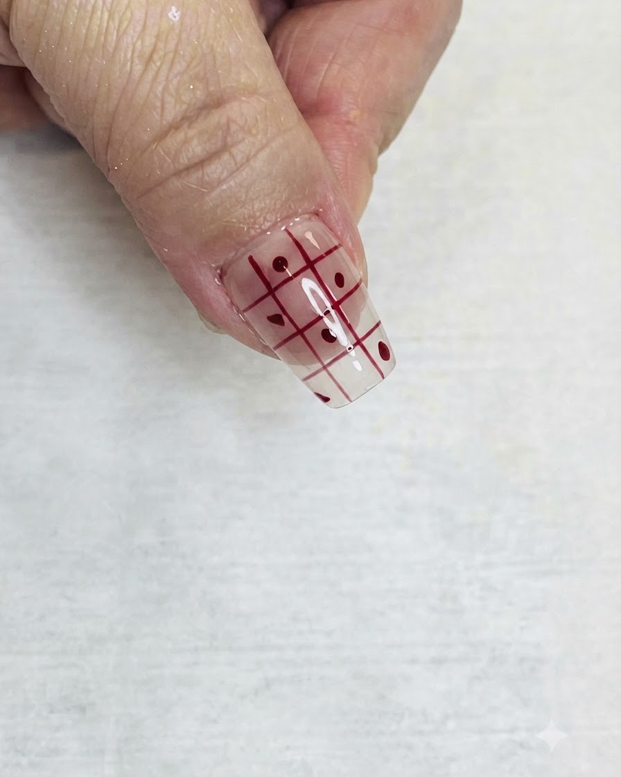 A fine liner brush filling in alternating squares of a red grid pattern on a clear nail with red polish.