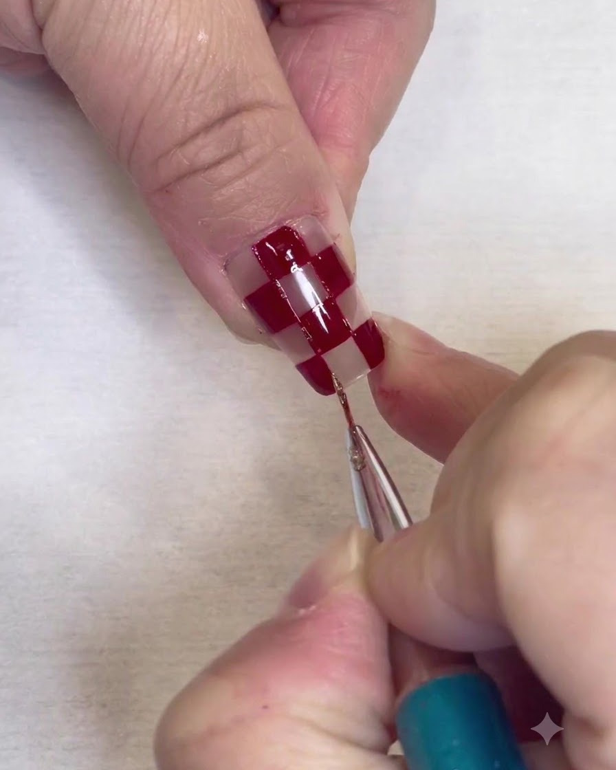 A fine detail brush painting thin silver glitter borders along the edges of red squares on a clear nail.