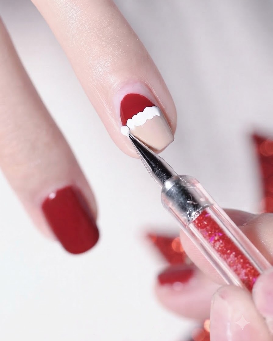 A close-up of a dotting pen placing a white dot at the tip of the red Santa hat.