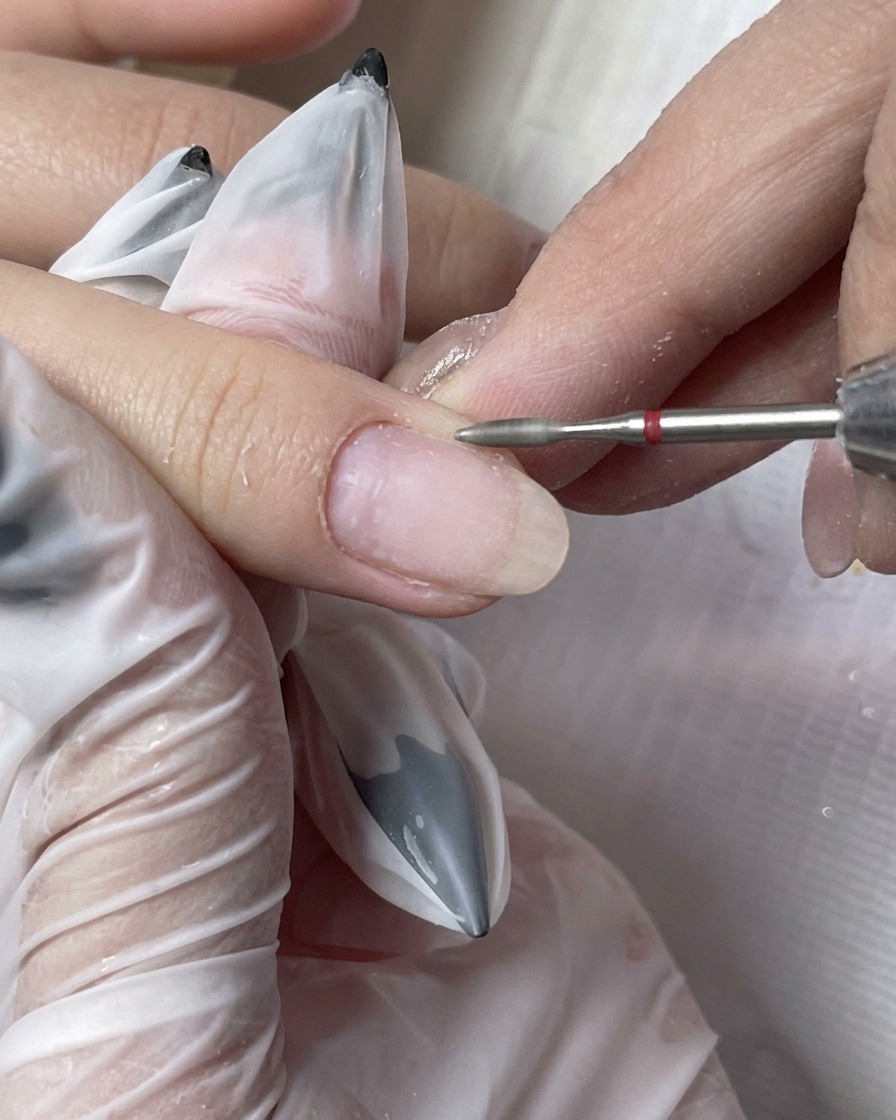 A dusting brush clearing away fine particles from a freshly prepped fingernail.