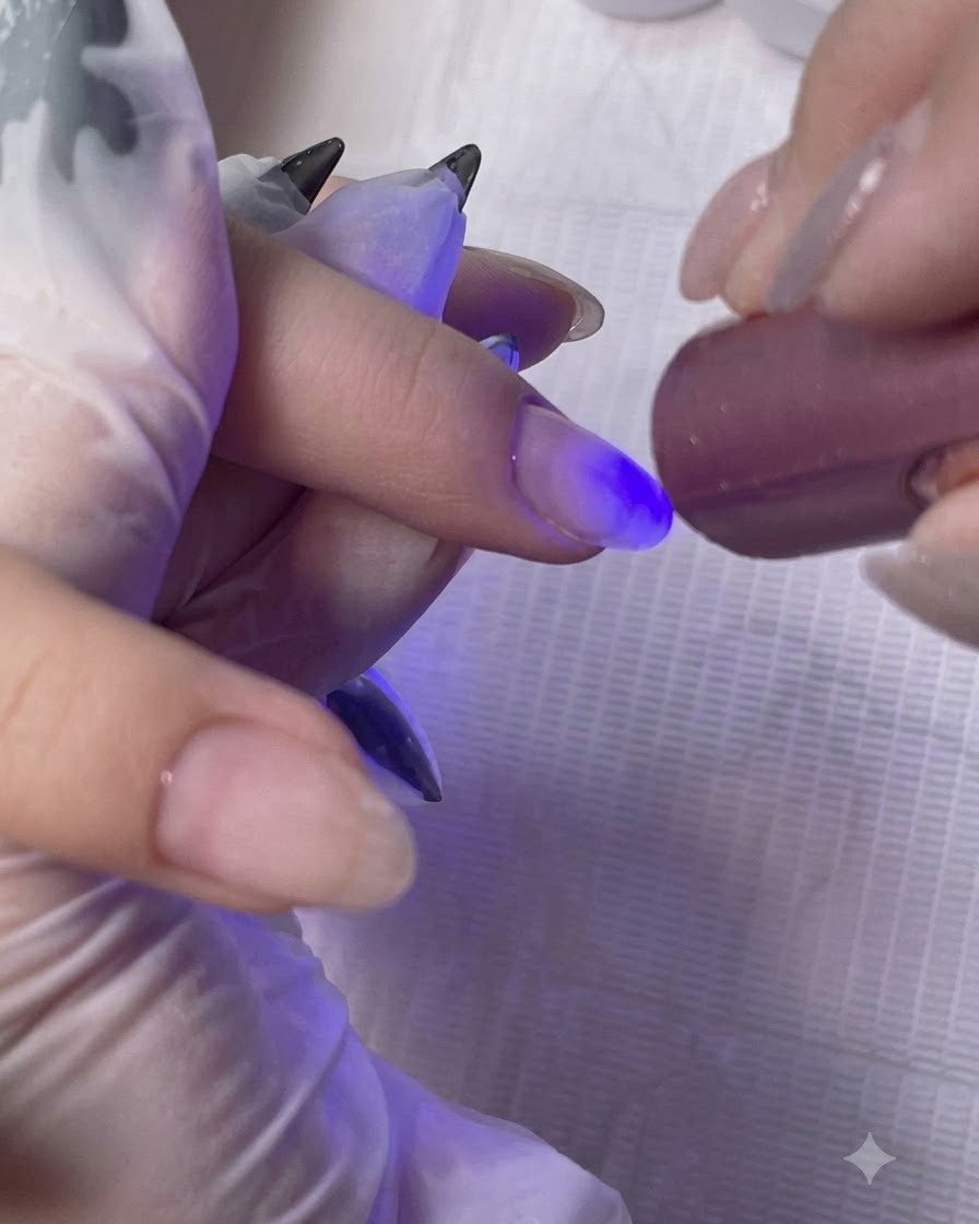 A mini handheld UV/LED lamp curing the base coat layer on a clients finger.