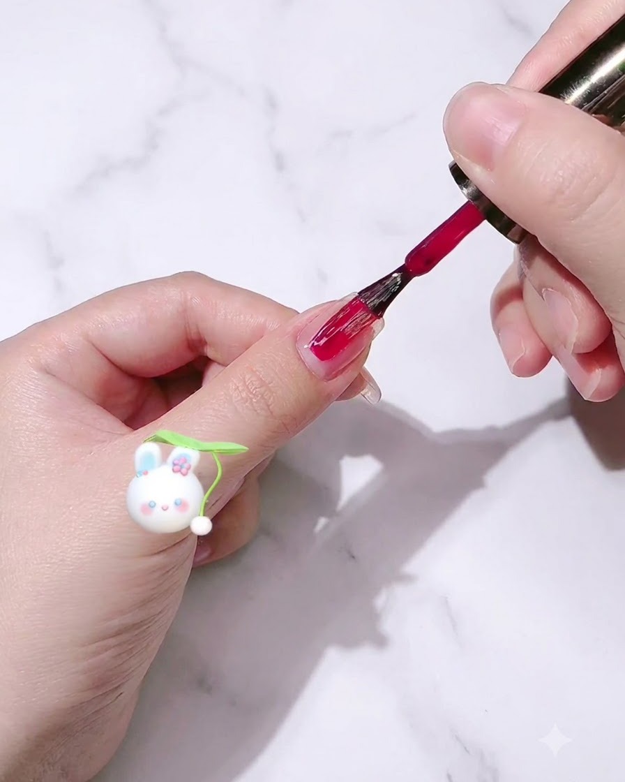 A nail polish brush applying rose red gel polish onto a fingernail.