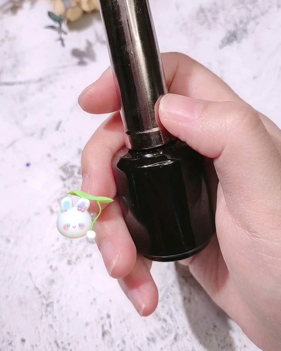A nail brush applying a matte top coat over a vibrant rose red colored fingernail.