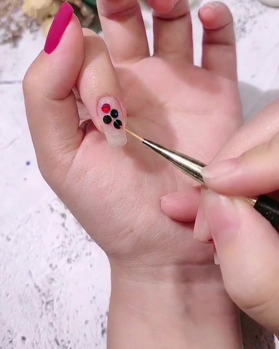 A close-up of a hand placing medium-sized colored dot sequins next to larger ones on a nail using a fine detail brush.