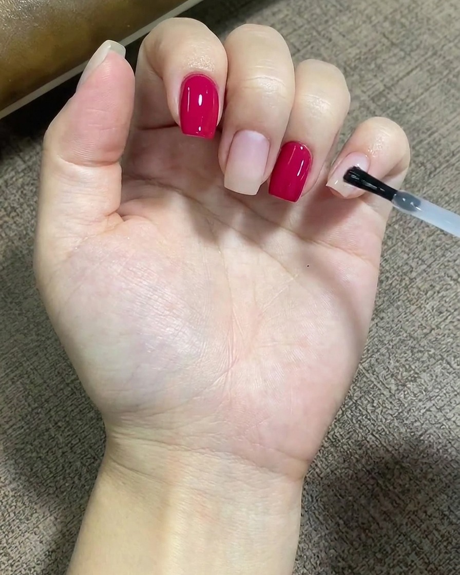 A brush applying a clear layer of base coat evenly over the surface of a fingernail.