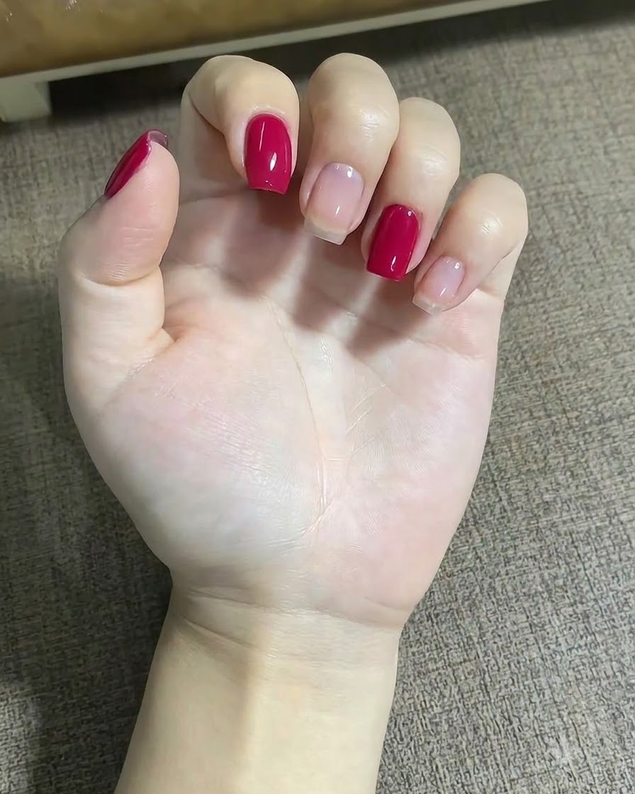 A close-up of a hand using a fine liner brush to apply small red dots near a star design on the middle finger.