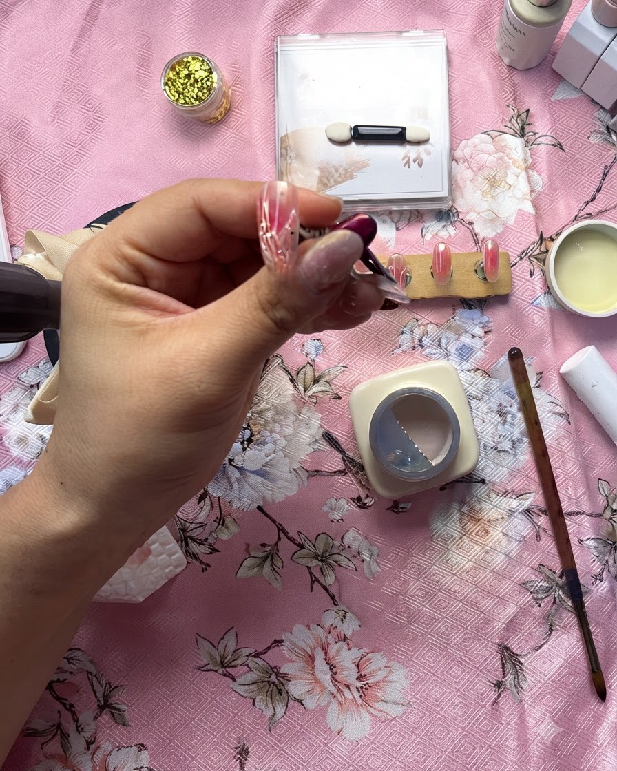 A detailed close-up of a nail artist using a fine brush to apply a raised clear gel line over a white heart design.